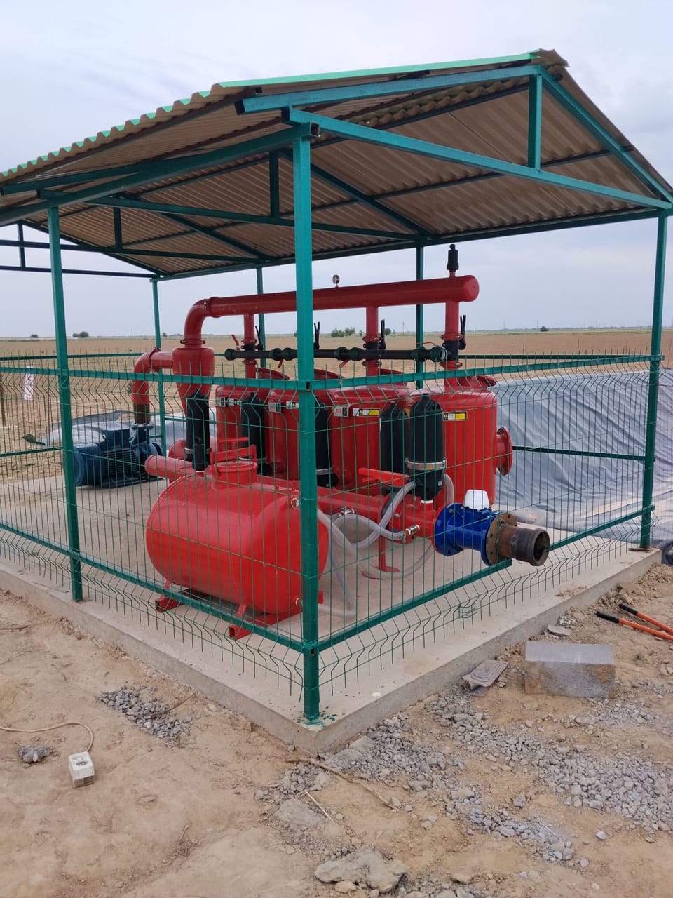 Stansiyaga yon tomondan qarash: qizil kollektor va ventillar, filtr idishlari, o‘g‘it baki hamda chiqish quvuridagi ko‘k suv hisoblagich.
